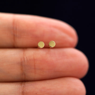 A model's hand holding a pair of recycled 14k gold Mini Circle Earrings