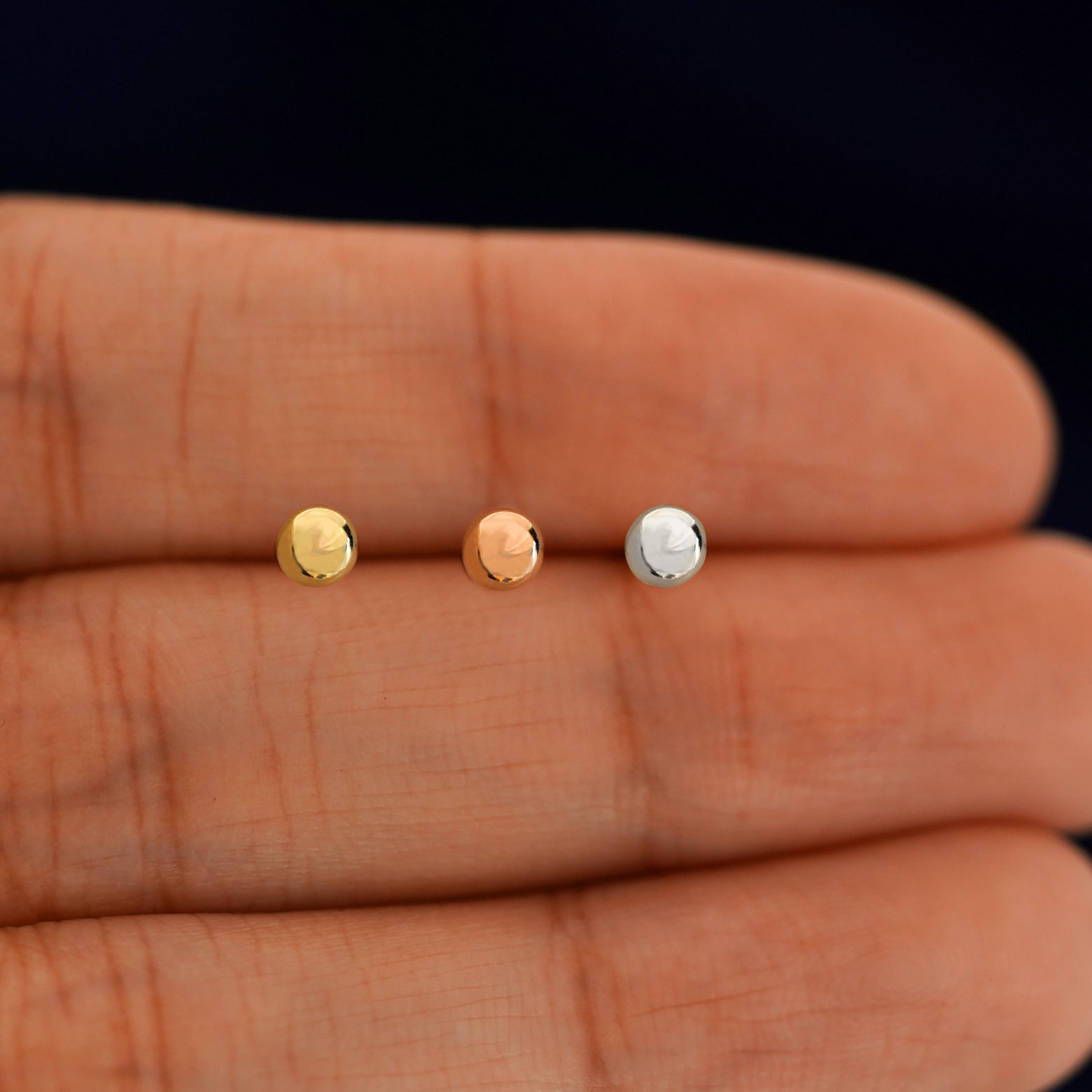 Three versions of the Medium Ball Flat Back showing options of yellow, rose, and white gold in between a model's fingers