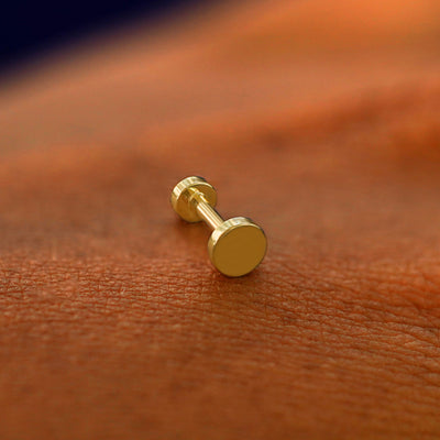 A solid 14k yellow gold Medium Circle Flatback Piercing resting on the back of a model's hand