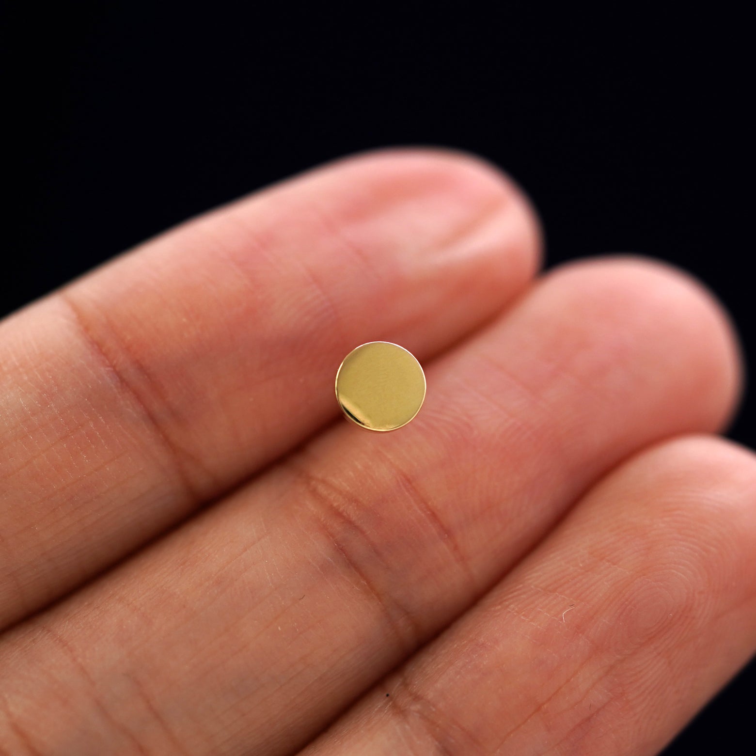 A solid 14k yellow gold Medium Circle Earring in between a model's fingers