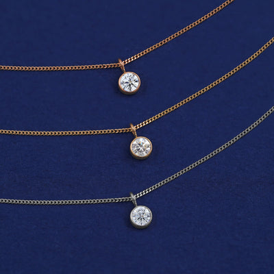 Three versions of the Moissanite Necklace shown in options of yellow, white and rose gold on a dark blue background