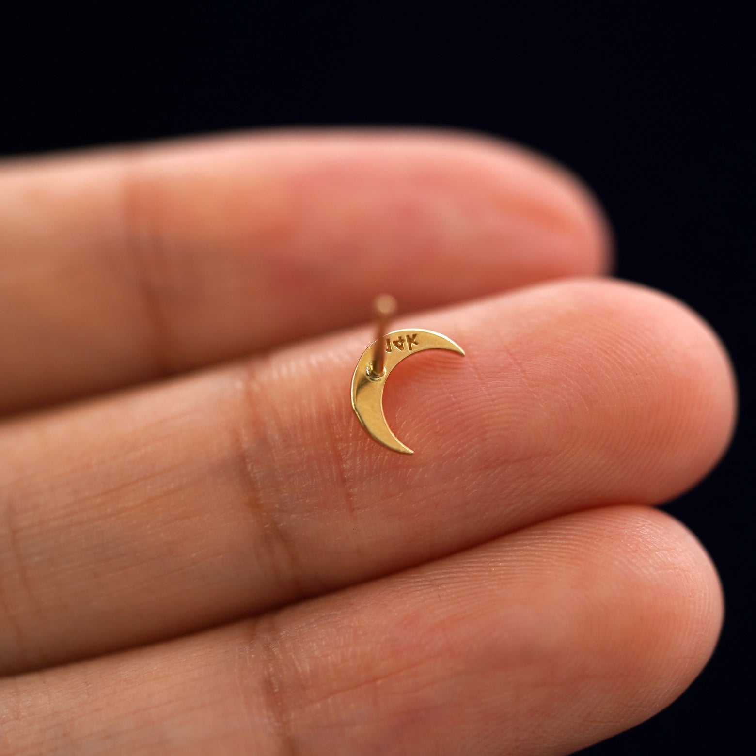 A yellow gold Moon Earring laying facedown on a model's fingers to show the underside view