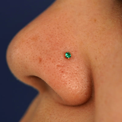 A model's nose wearing a 14 karat gold emerald Nose Stud