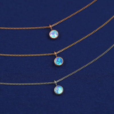 Three versions of the Opal Necklace shown in options of yellow, white and rose gold on a dark blue background