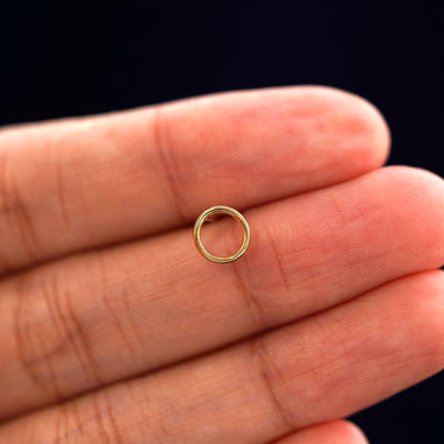 A solid 14k yellow gold Open Circle Earring in between a model's fingers