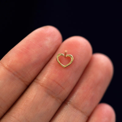 A yellow gold Heart Earring laying facedown on a model's fingers to show the underside view