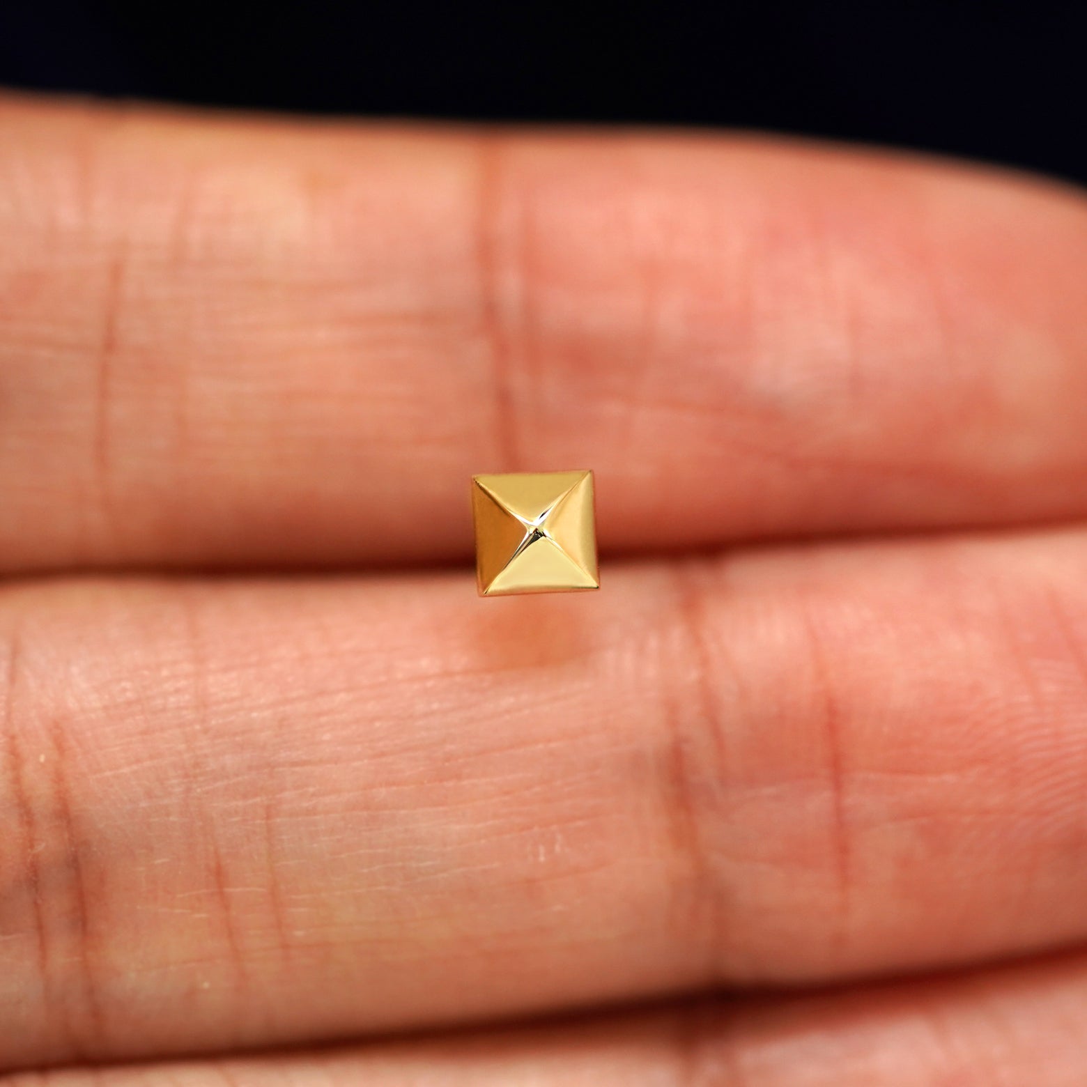 A solid 14k yellow gold Pyramid Earring in between a model's fingers