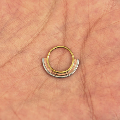 A model's hand holding a 14 karat yellow gold Pierced Rainbow Septum