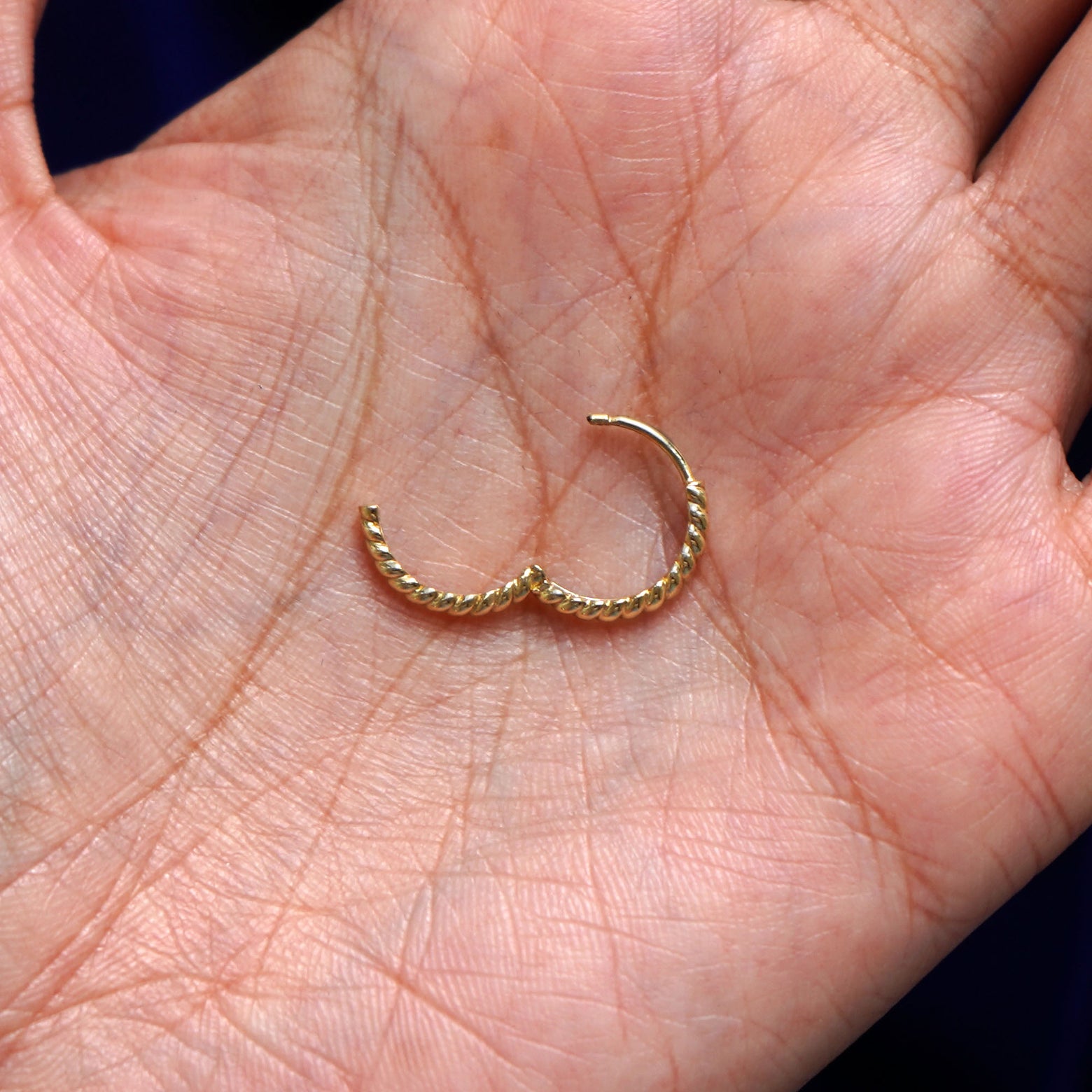 A solid 14k yellow gold Medium Rope Huggie Hoop Earring open in a model's palm to show the hinge