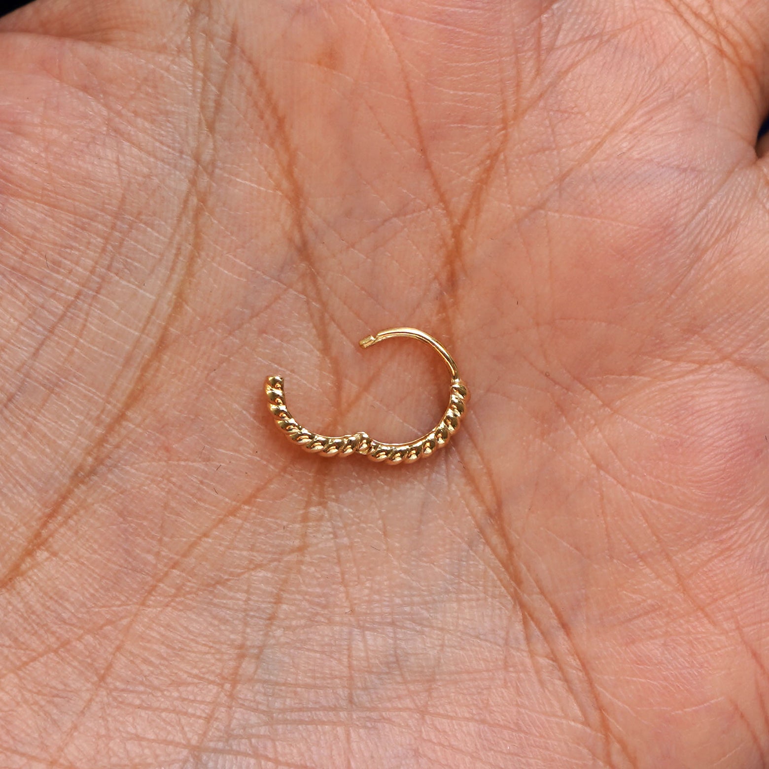 A solid 14k yellow gold Mini Rope Huggie Hoop Earring open in a model's palm to show the hinge