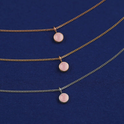 Three versions of the Rose Quartz Necklace shown in options of yellow, white and rose gold on a dark blue background