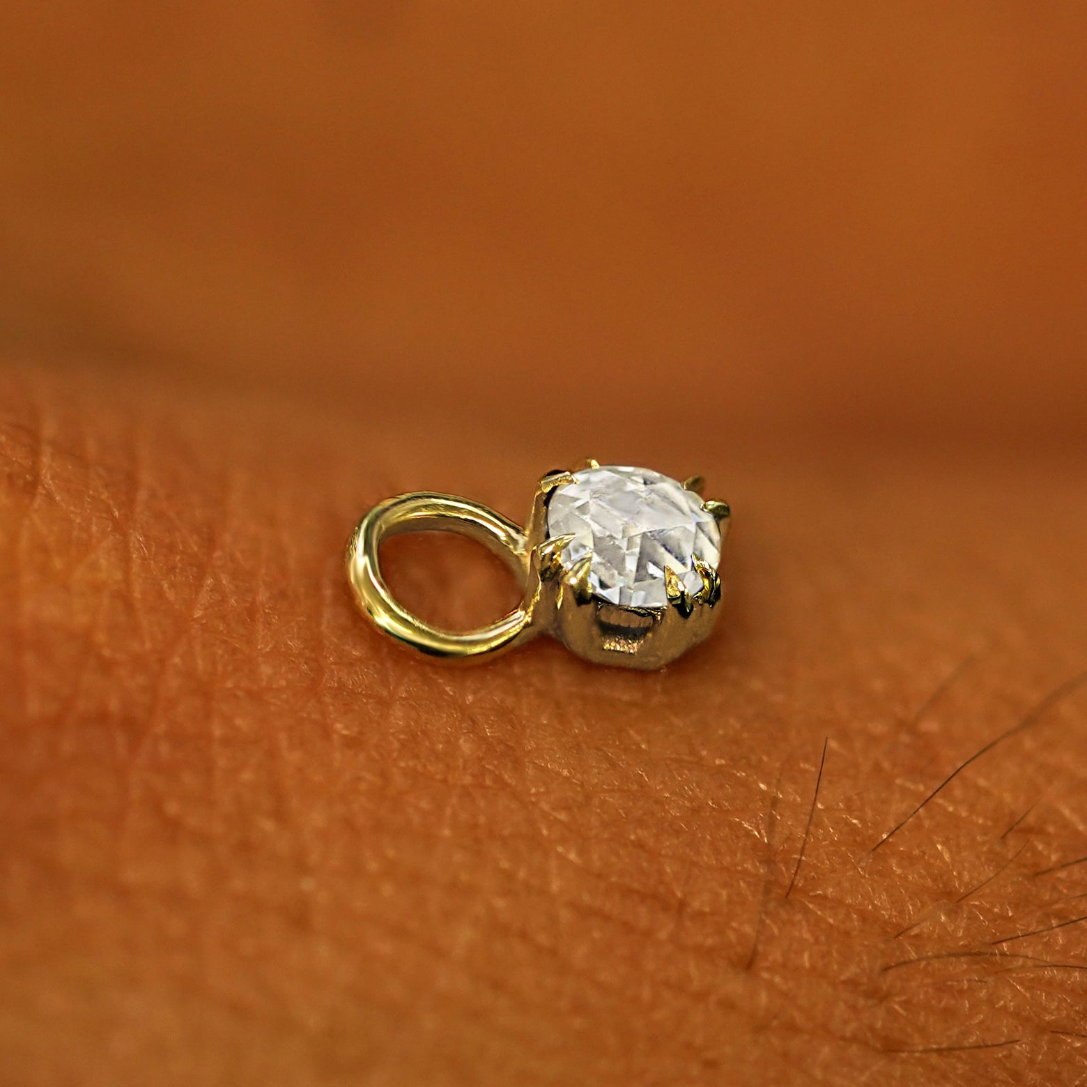 A solid yellow gold Rose Cut Diamond Charm for earring resting on the back of a model's hand