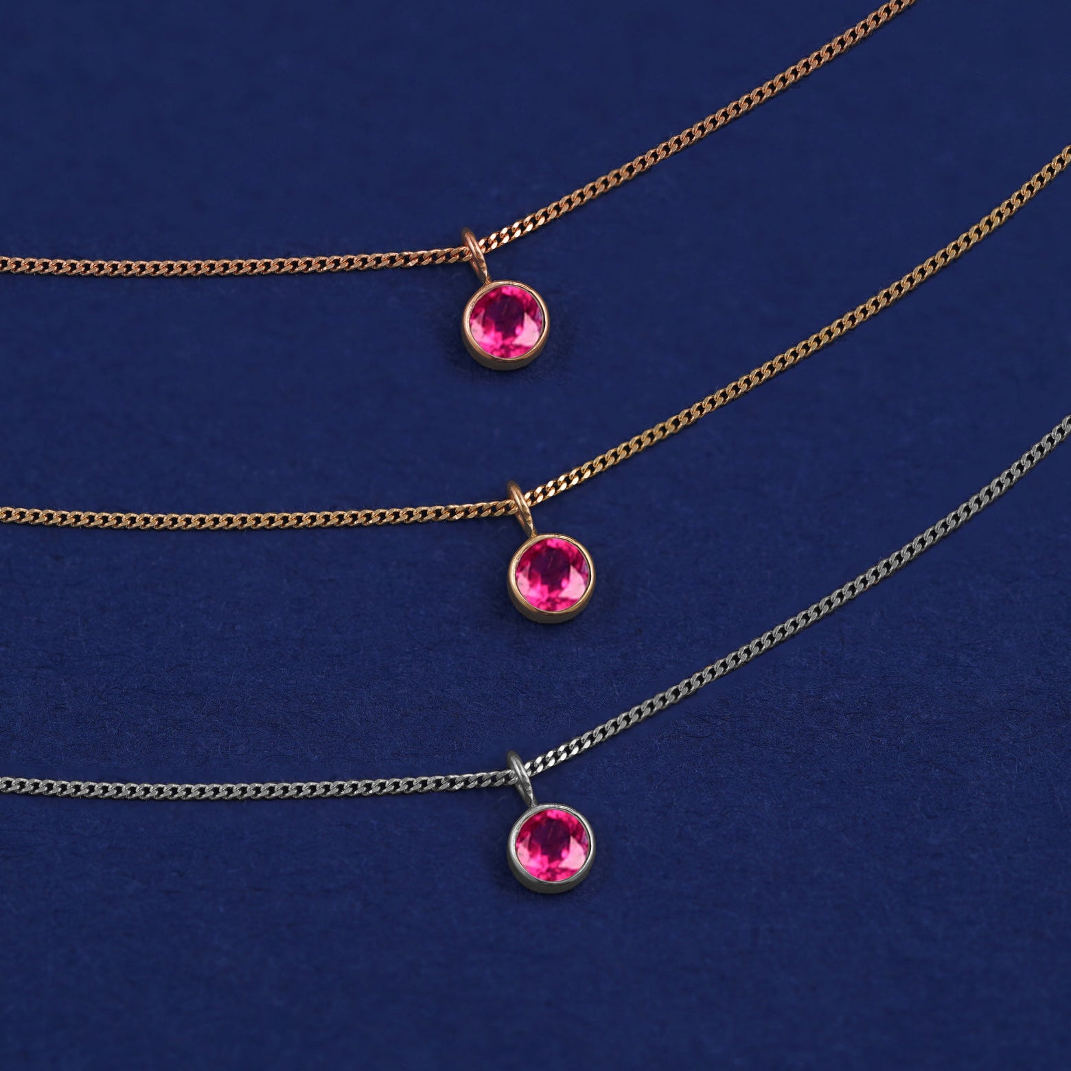 Three versions of the Ruby Necklace shown in options of yellow, white and rose gold on a dark blue background