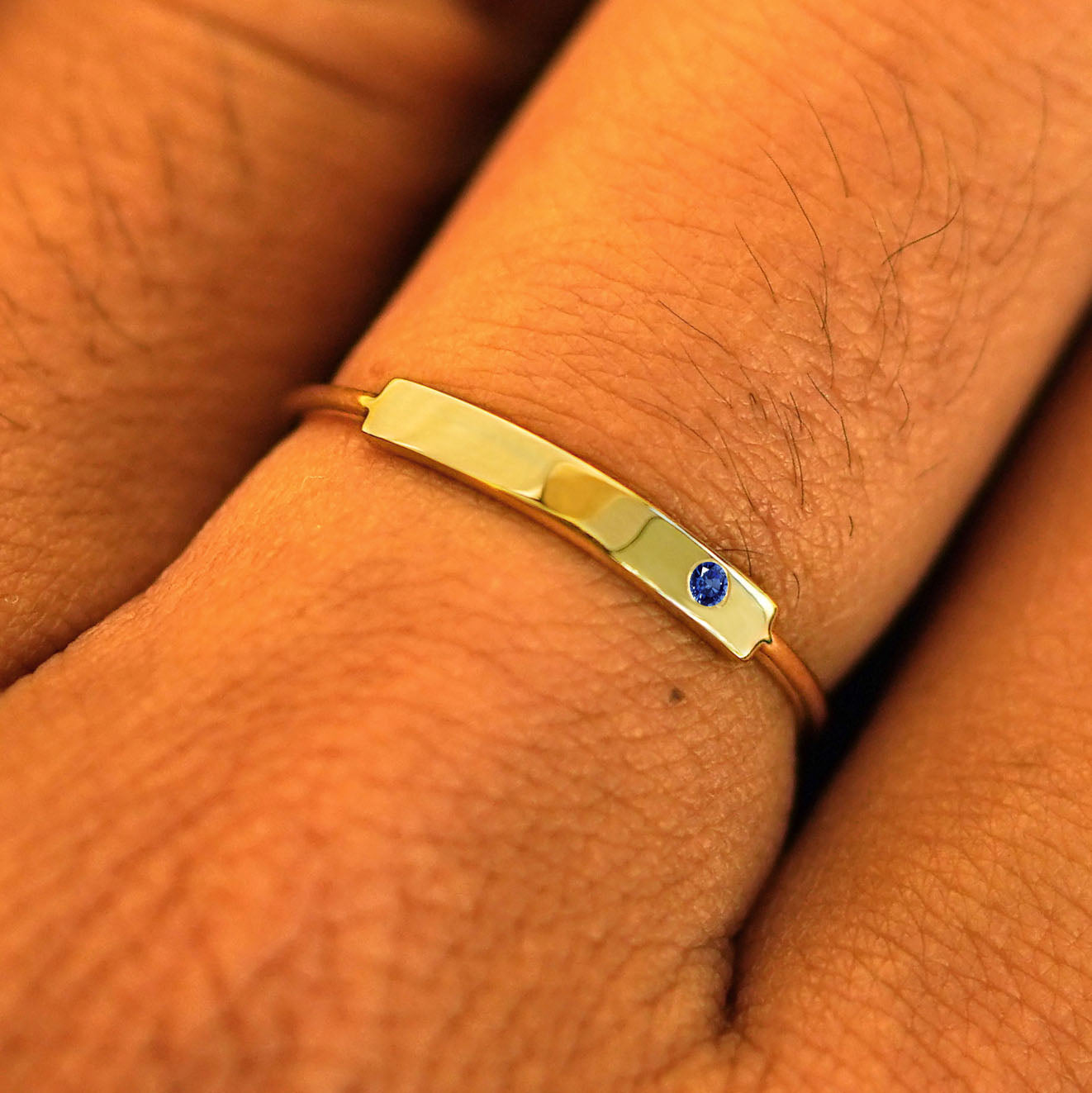 Close up  view of a model's fingers wearing a 14k yellow gold sapphire Gemstone Bar Ring