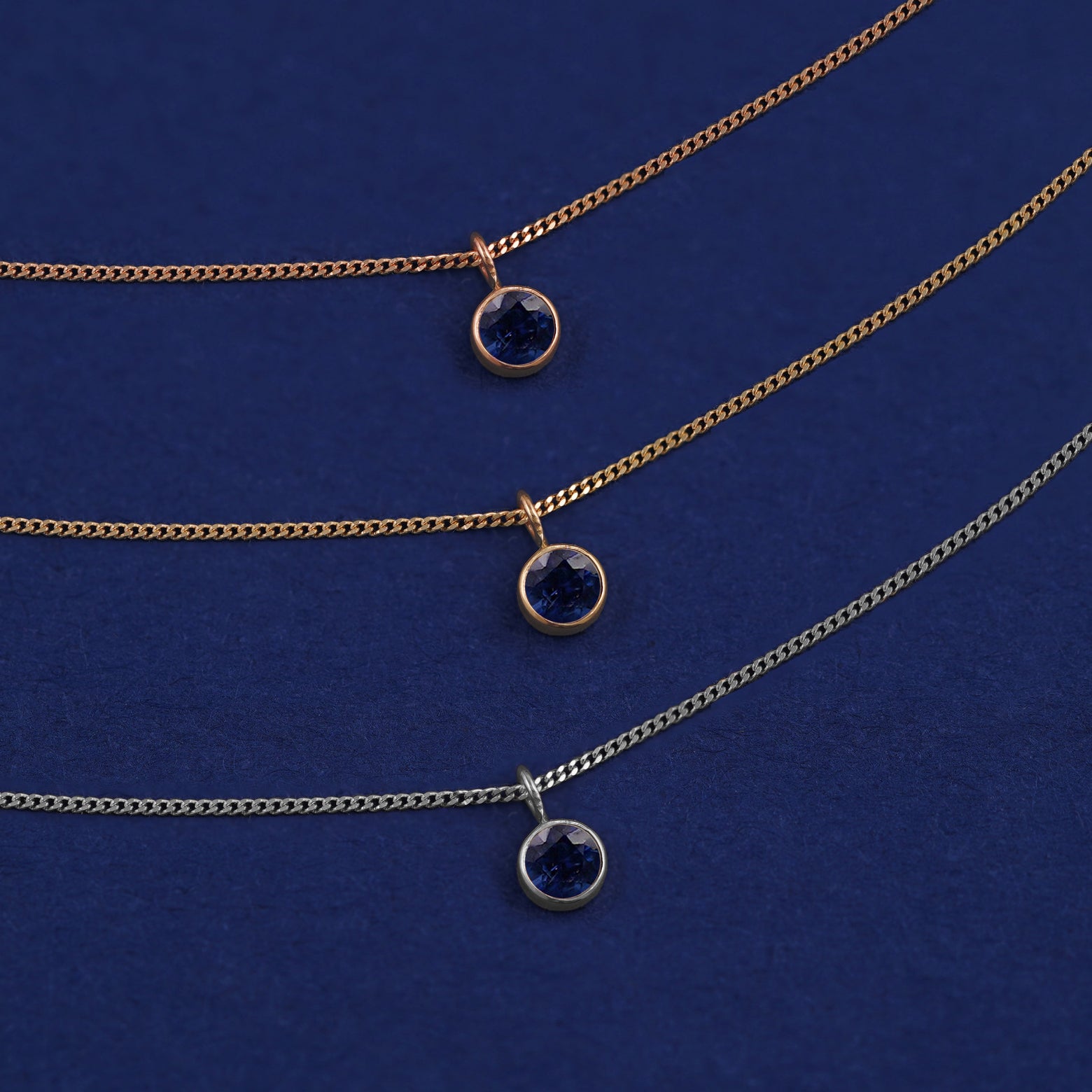 Three versions of the Sapphire Necklace in options of yellow, white, and rose gold on a dark blue background