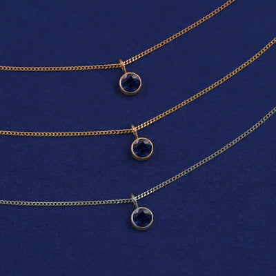 Three versions of the Sapphire Necklace in options of yellow, white, and rose gold on a dark blue background