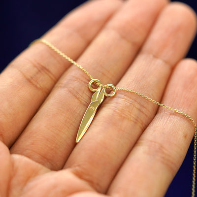 A yellow gold Scissors Necklace resting on a model's fingers with the scissors shown closed