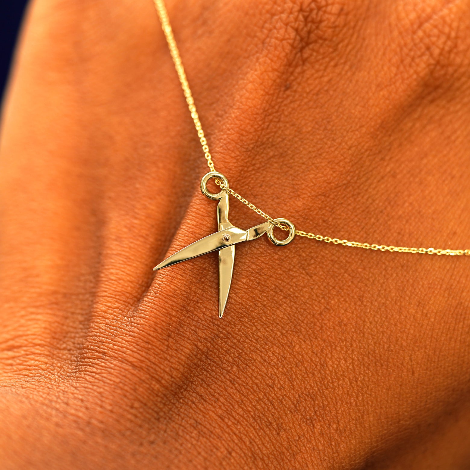 A solid gold Scissors Necklace resting on the back of a model's hand with the scissors shown open