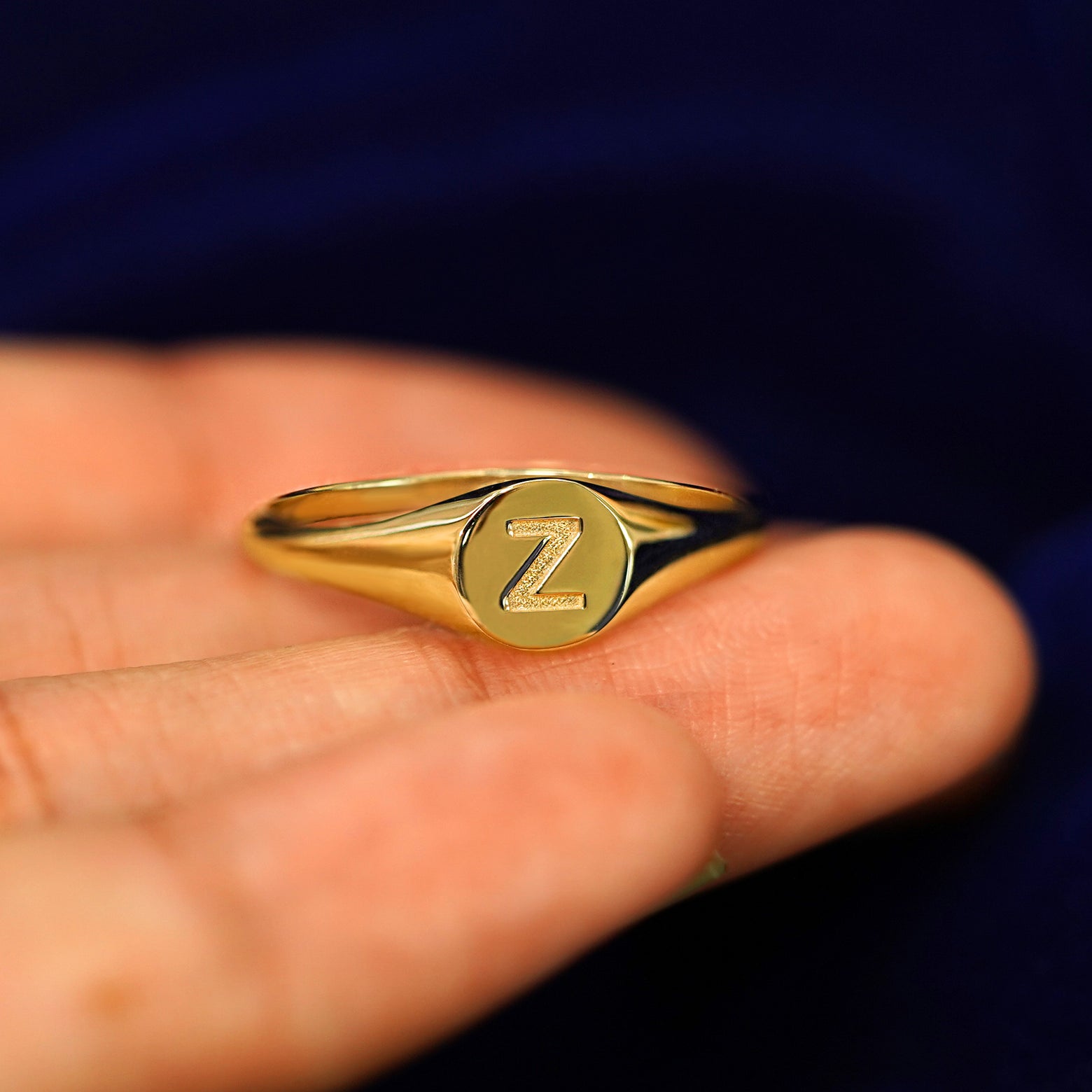 A yellow gold Signet Ring in a model's hand with the letter Z engraved on top in a classic block font