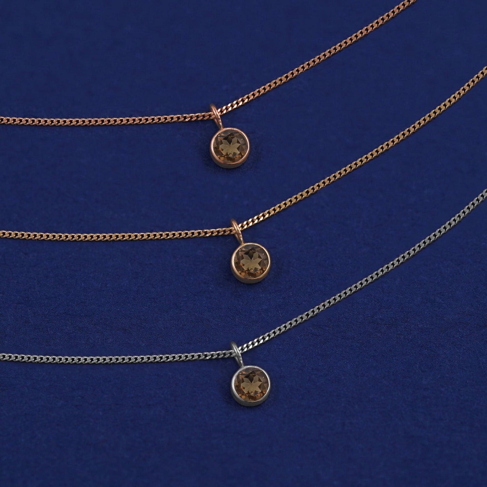 Three versions of the Smoky Quartz Necklace in options of yellow, white, and rose gold on a dark blue background