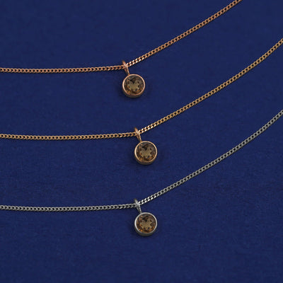 Three versions of the Smoky Quartz Necklace in options of yellow, white, and rose gold on a dark blue background