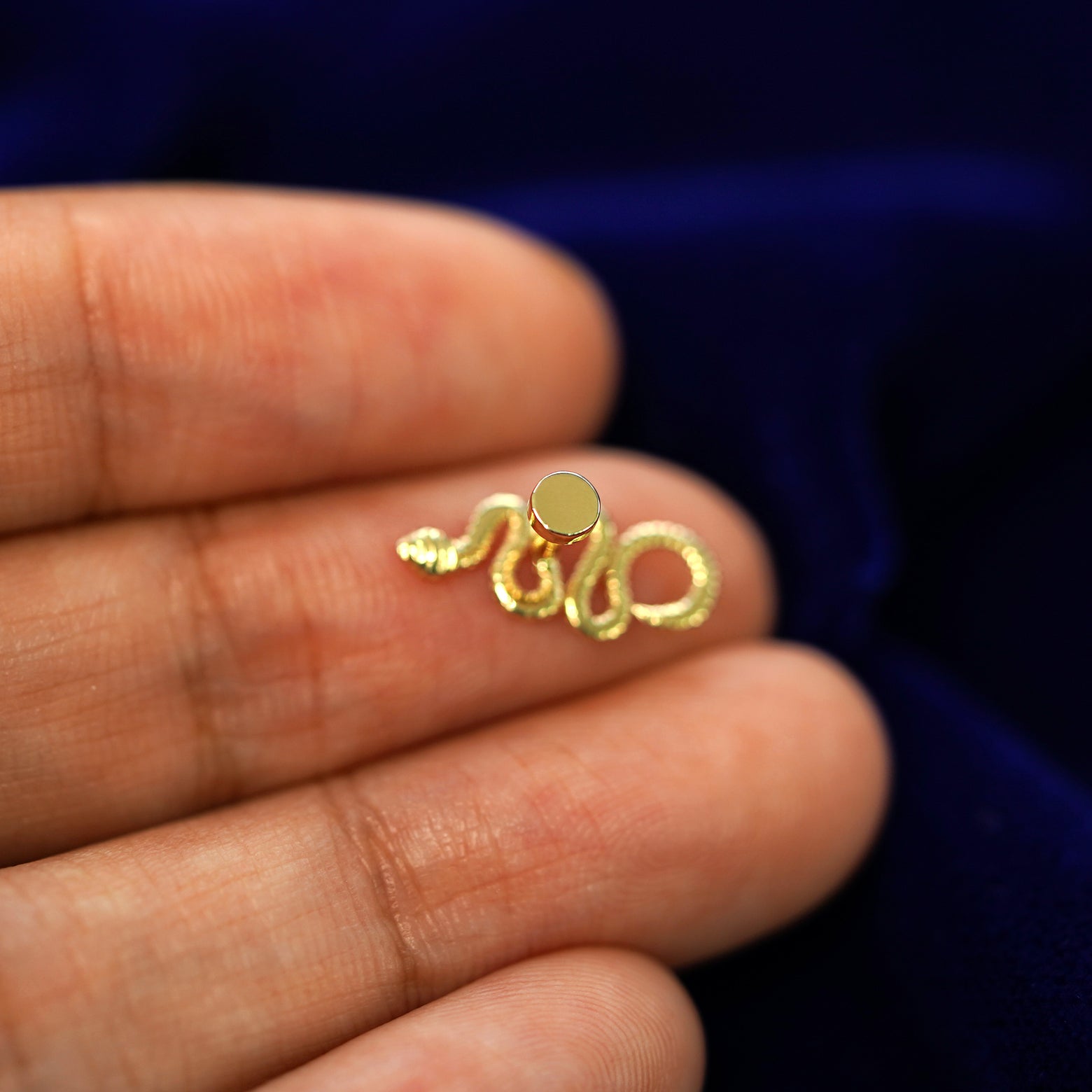 A solid yellow gold Snake Flatback Piercing laying facedown on a model's finger to show the end of the flat back