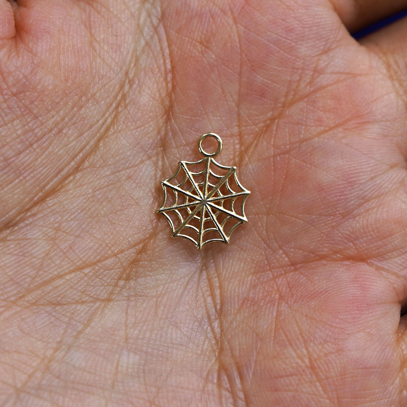 A solid gold Spider Web Charm for earring resting in a model's palm