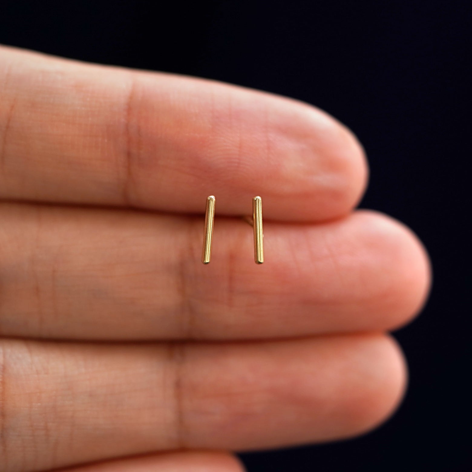 A model's hand holding a pair of recycled 14k gold Medium Line Earrings