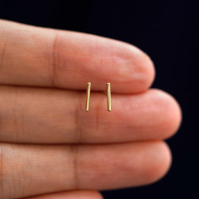 A model's hand holding a pair of recycled 14k gold Medium Line Earrings