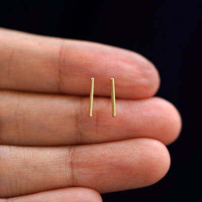 A model's hand holding a pair of recycled 14k gold Large Line Earrings