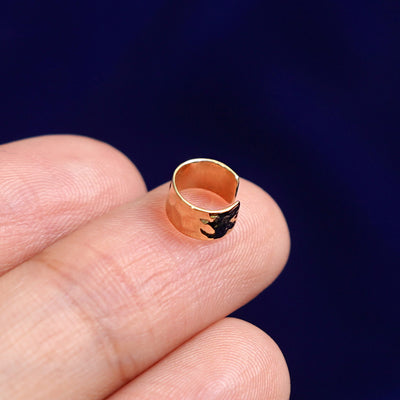 A solid yellow gold Thick Hammered Cuff earring resting on a model's fingertips