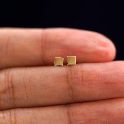 A model's hand holding a pair of recycled 14k gold Square Earrings