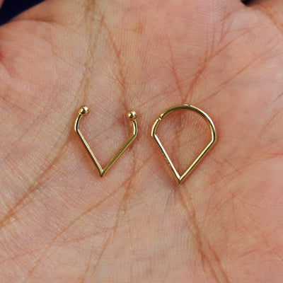 Two 14k solid gold Triangle Septum rings show in options of Non-Pierced and Pierced resting in the palm of a model's hand