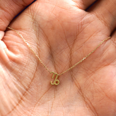 A yellow gold Capricorn Horoscope Necklace draped on a model's palm