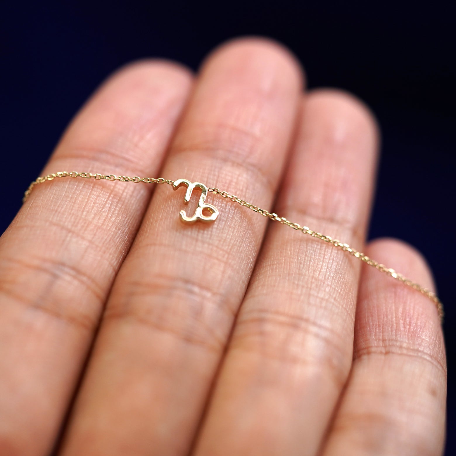 A yellow gold Capricorn Horoscope Necklace resting on a model's fingers