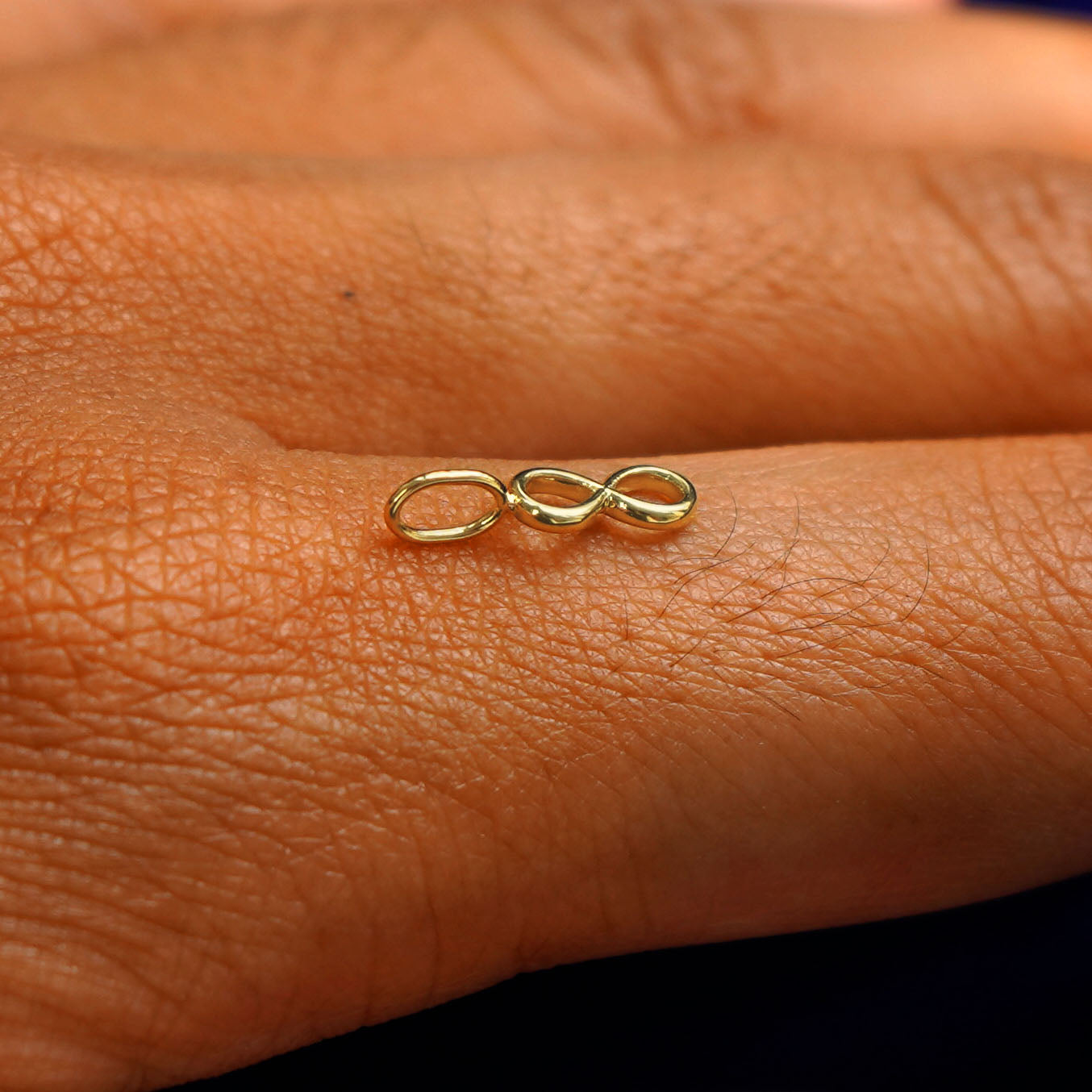 A 14k yellow gold Infinity Charm for chain balancing on the back of a model's finger