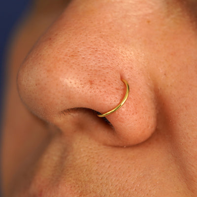 Side view of a model's nose wearing a 14k yellow gold Nose Ring Hoop