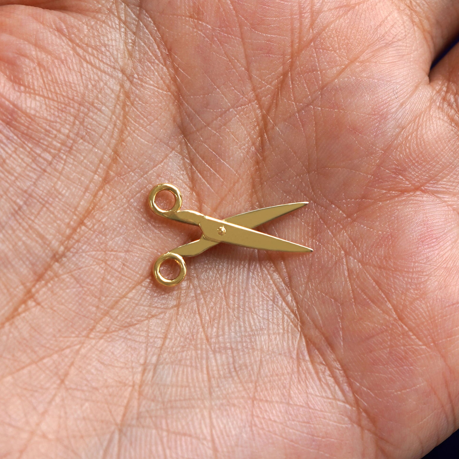A solid gold Scissors Charm for earring resting in a model's palm