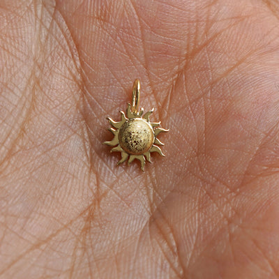 A solid gold Sun Charm for chain resting in a model's palm