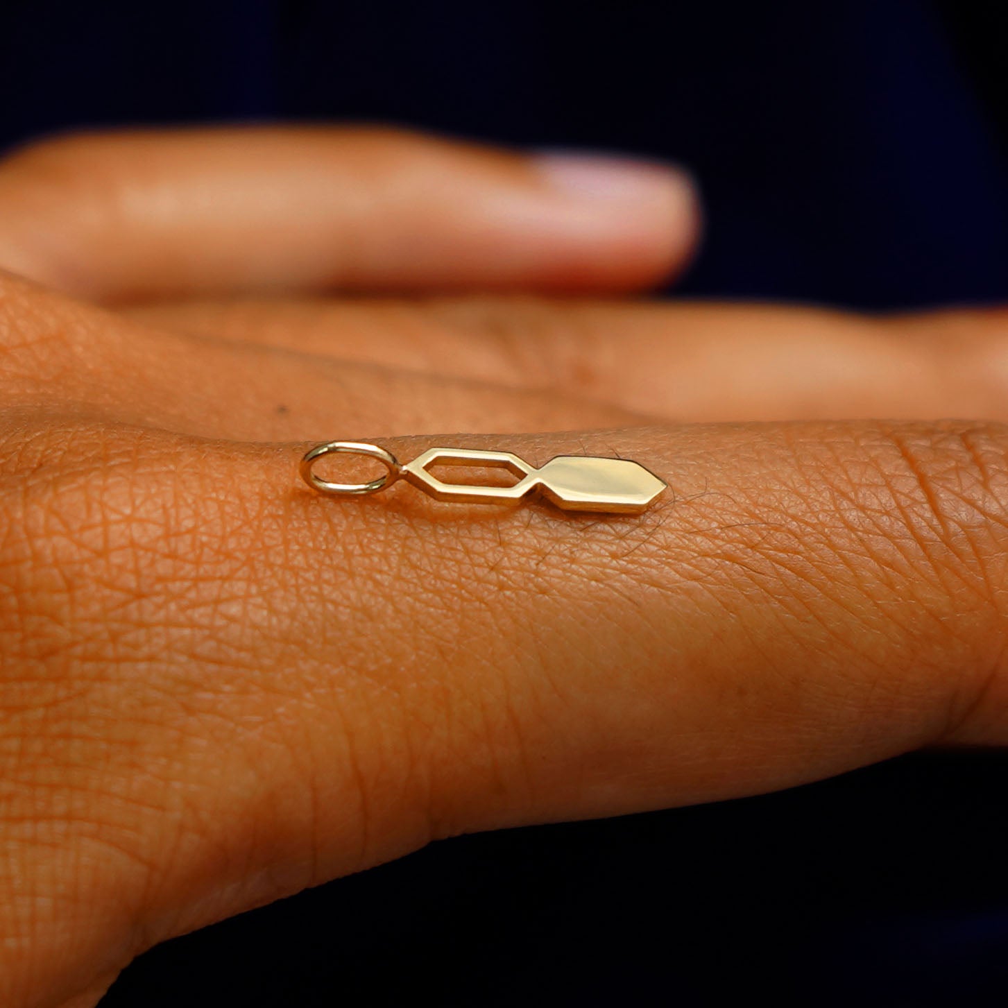 A 14k yellow gold Tanlah Charm for chain balancing on the back of a model's finger