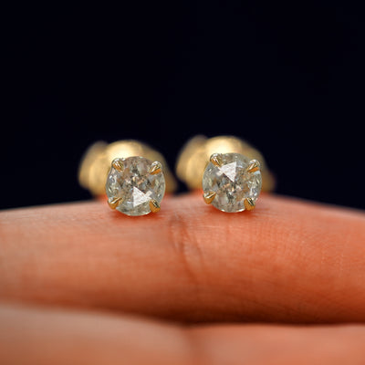 A pair of solid yellow gold Salt and Pepper Diamond Pressure Lock Earrings resting on a model's fingertip