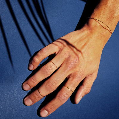 Close up view of a model's hand wearing a Line Bangle, a Bead Chain Ring, a Line Ring, and a Wave Ring in yellow gold