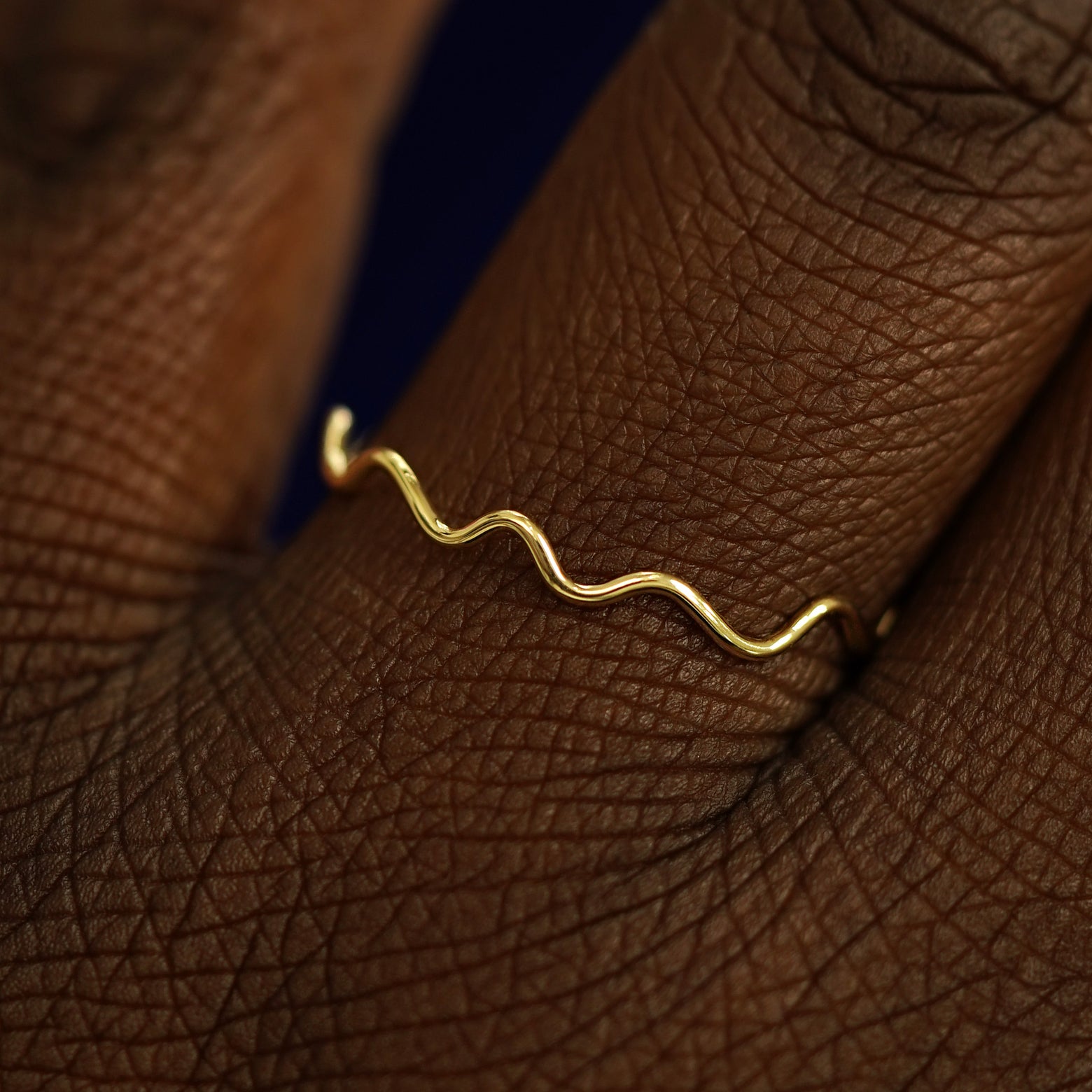 Close up view of a model's hand wearing a solid yellow gold Wave Ring