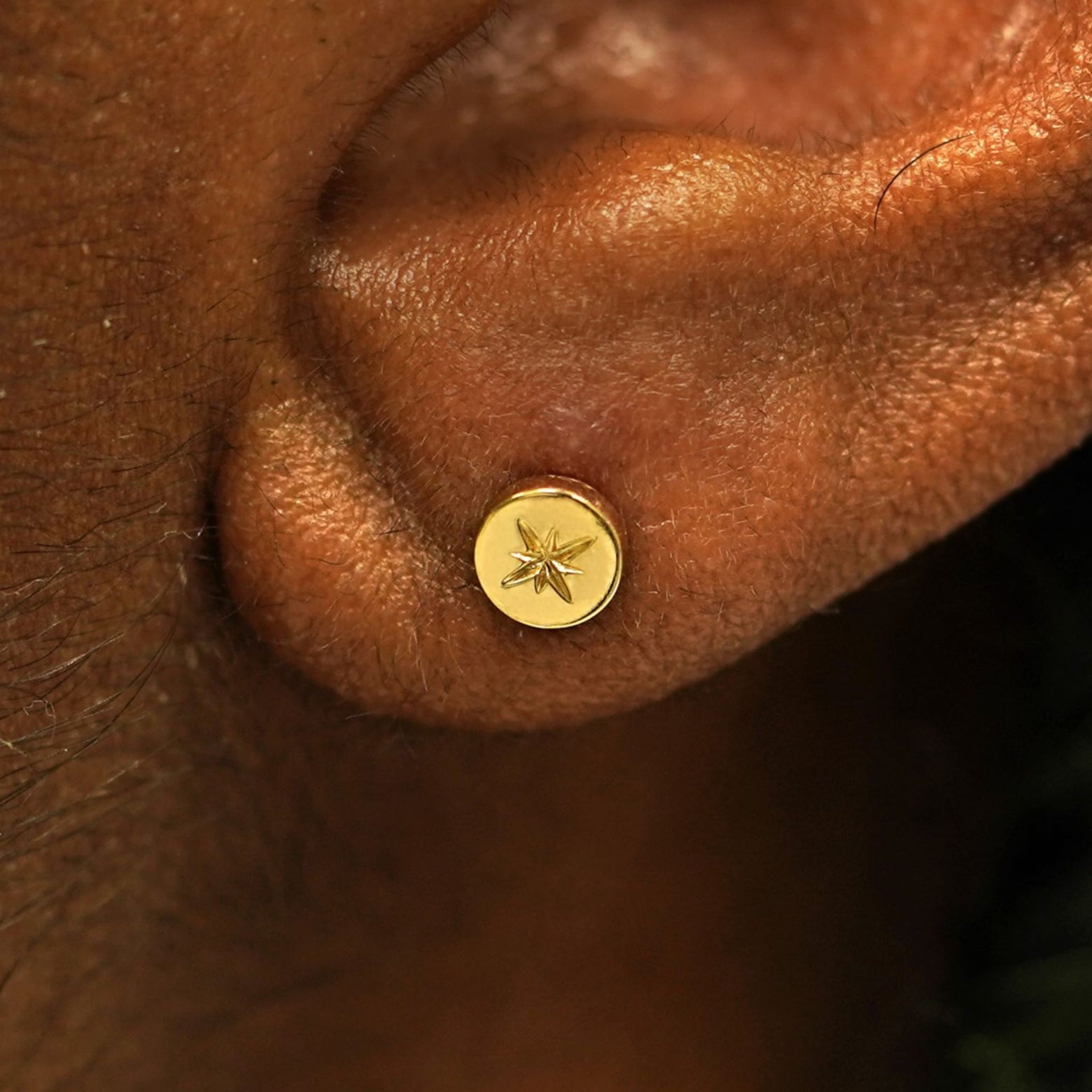 Close up view of a model's ear wearing a solid 14k gold Star Disc Earring