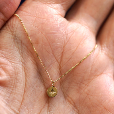 A yellow gold Star Disk Necklace draped on a model's palm