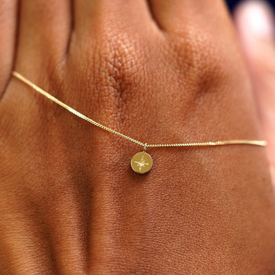 A solid gold Star Disk Necklace resting on the back of a model's hand