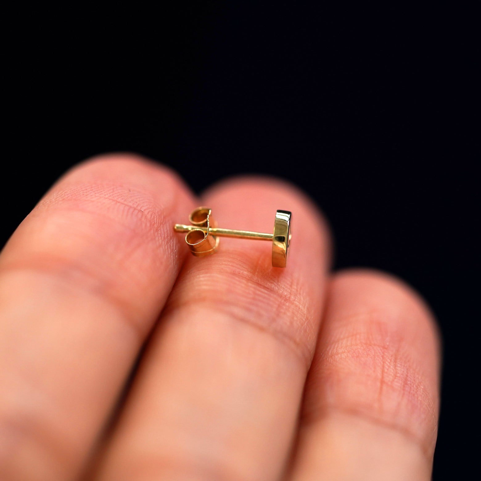 A 14k gold Star Disk Earring sitting sideways on a model's fingertips to show detail