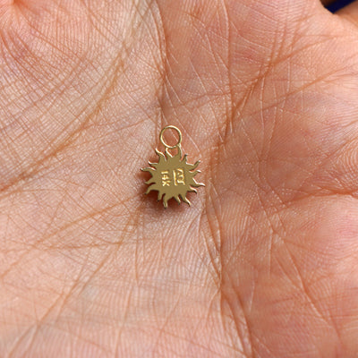 A 14k gold Sun Charm for chain resting in a model's palm to show the back of the charm