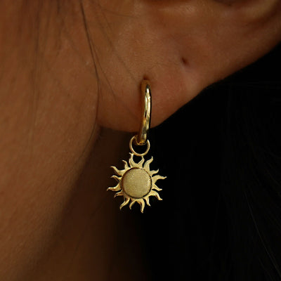 Close up view of a model's ear wearing a yellow gold Sun Charm on a Curvy Huggie Hoop