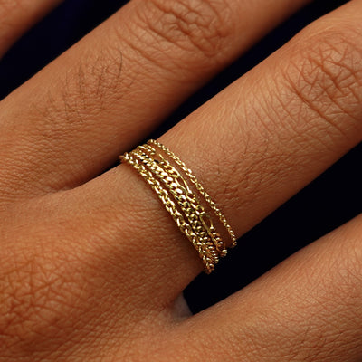 Close up view of a model's hand wearing a Cable Ring, a Figaro Ring, a Mini Miami Ring, and a Thick Cable Ring
